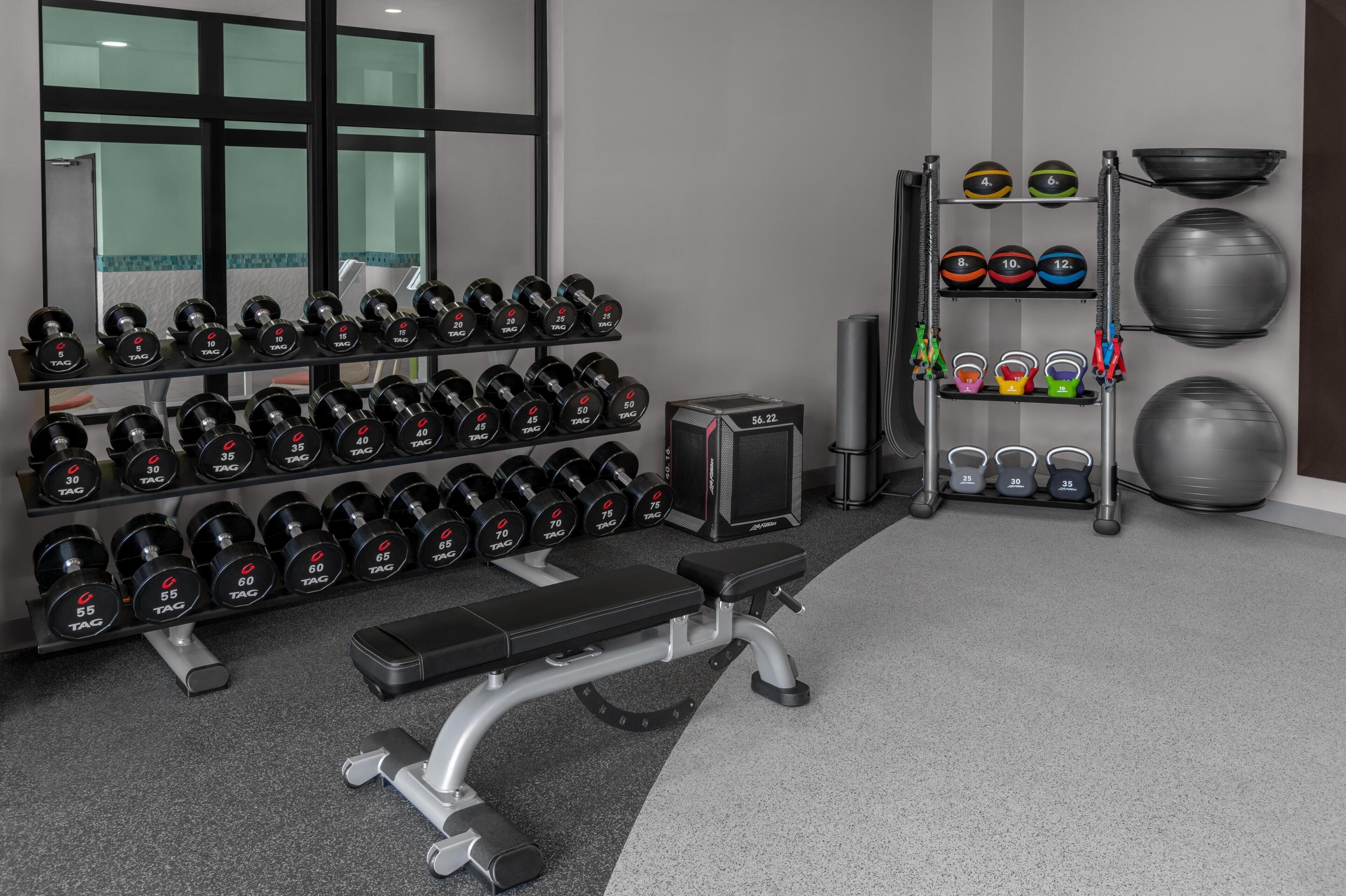 A gym with weight racks, dumbbells, a bench, and exercise balls.