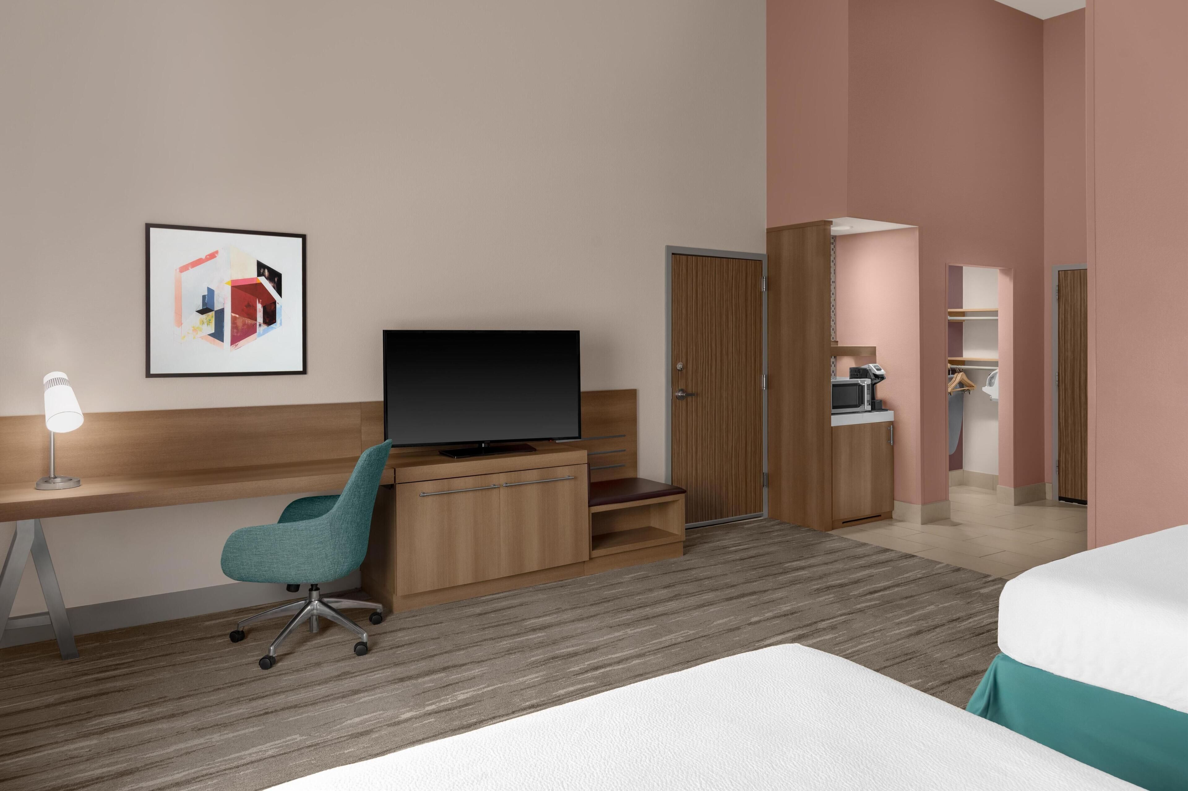 Een hotelkamer met een bed, een bureau met stoel, een televisie, een kledingkast en een badkamer zichtbaar door een geopende deur.