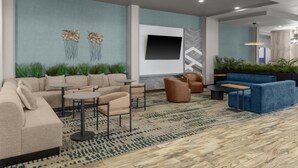 A modern lounge area with a sectional sofa, armchairs, a flat-screen TV, and decorative wall art. - Hilton Garden Inn Topeka (Topeka)