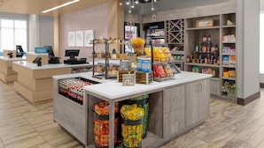Zona de recepción de hotel con mostrador, computadora y varios servicios, incluyendo una tienda y dispensadores de aperitivos.