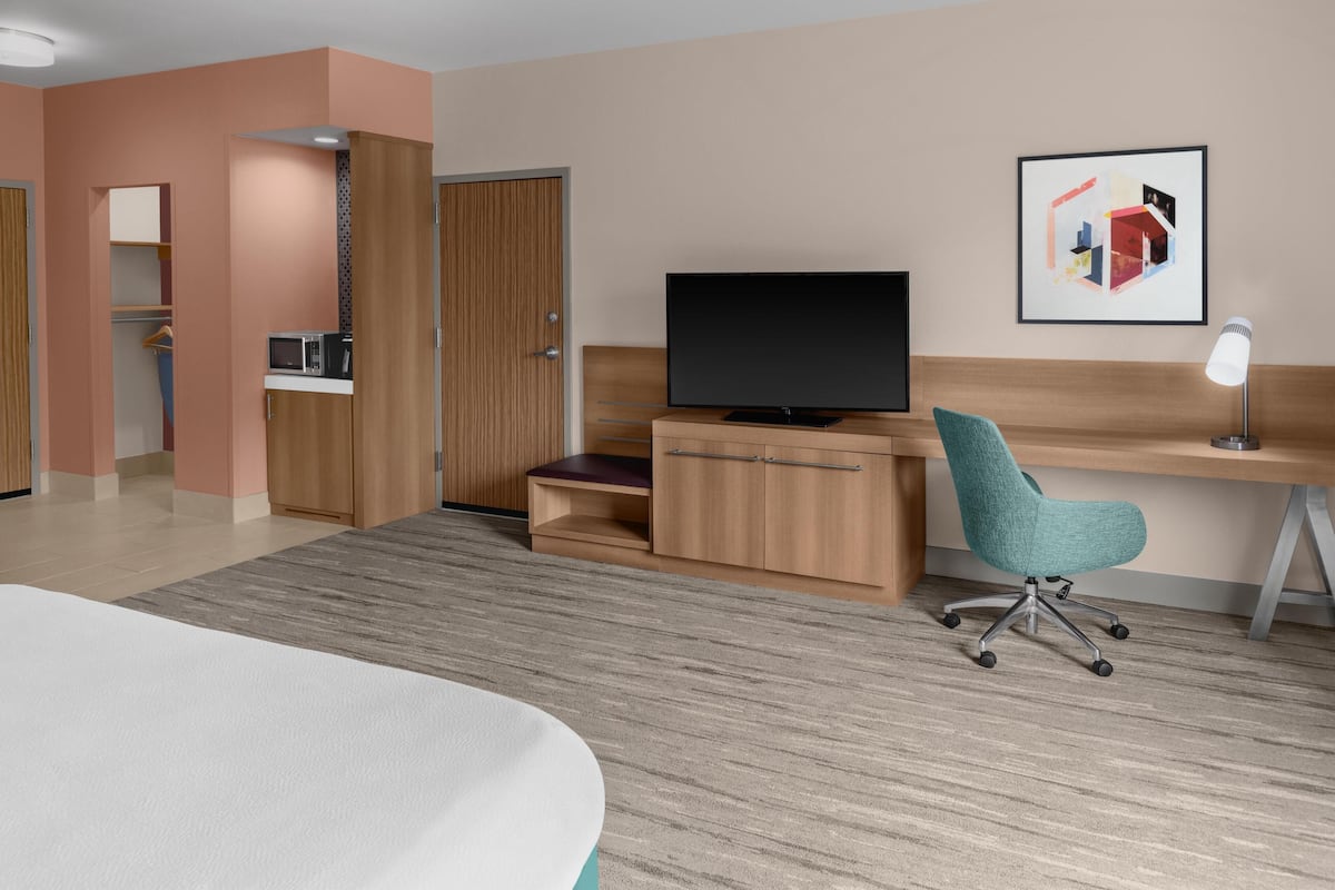 A hotel room with a bed, a desk with a computer, a TV, a chair, and a microwave.