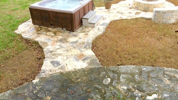 Een hottub met een terras van natuursteen, een vuurkuil en een stenen muur.