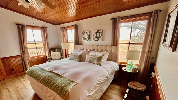 Un grand lit recouvert d’un plaid vert, un plafond en bois et une vue sur l’extérieur par les fenêtres.