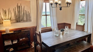 Un coin repas avec une table en bois, des chaises, un lustre et une œuvre d’art représentant un cactus accrochée au mur.