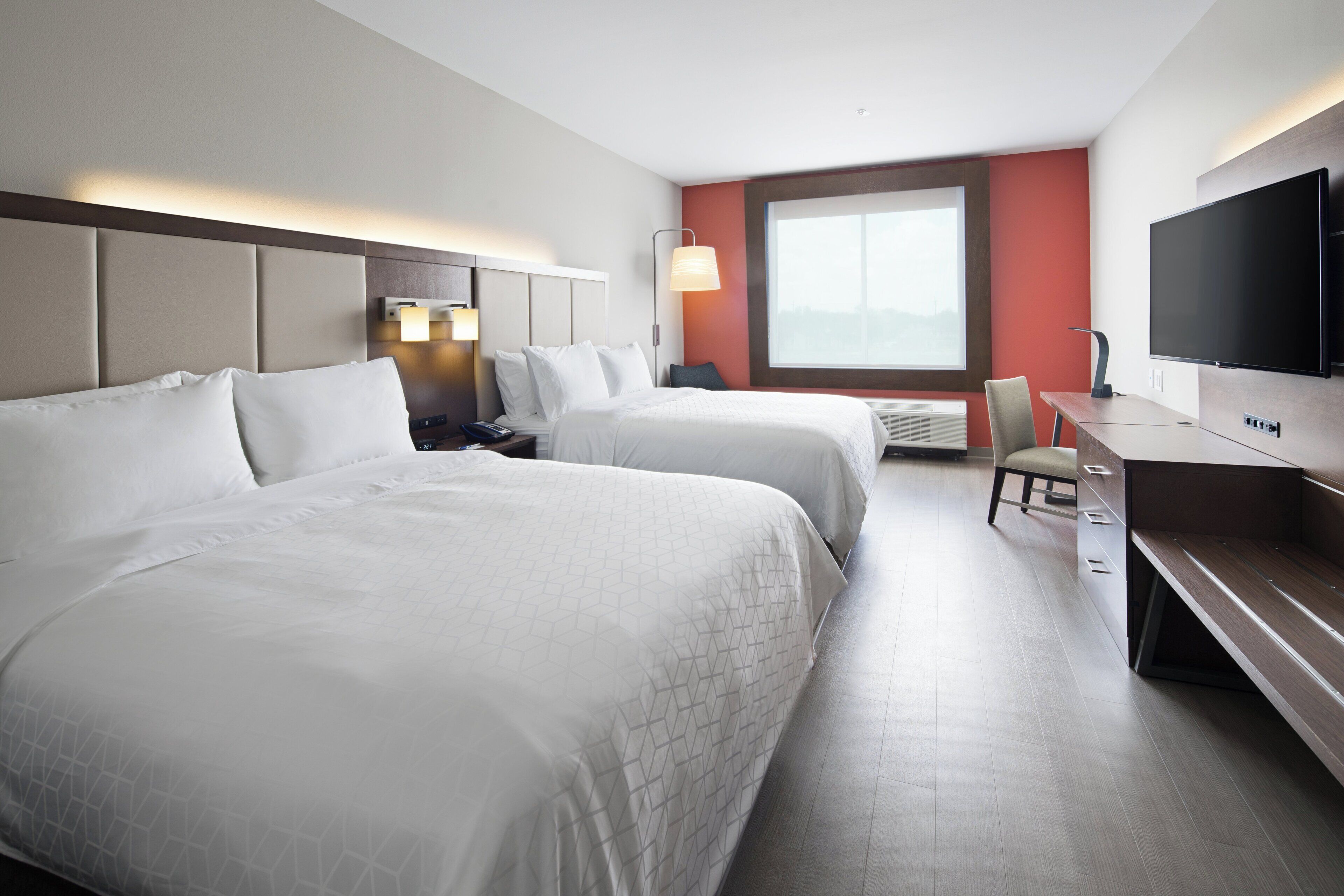A hotel room with two beds, a desk, a TV, and a large window.