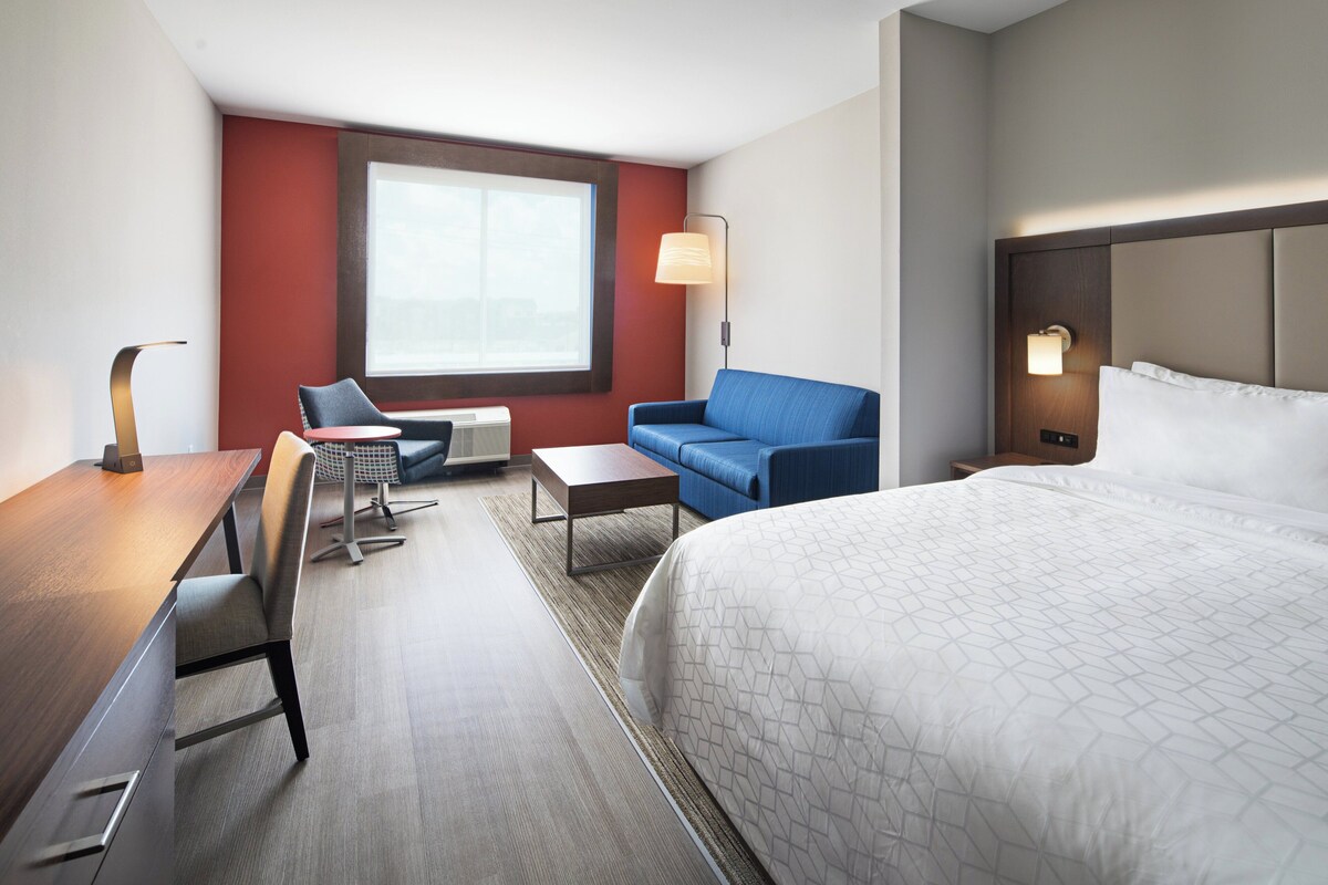 A hotel room with a bed, a desk, a chair, a sofa, a lamp, and a window.