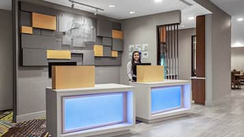 A reception area with a modern design, featuring a reception desk, a wall-mounted information board, and a patterned carpet.