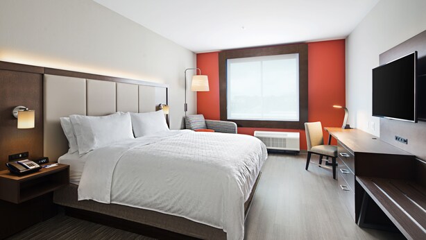 A modern hotel room with a large bed, a desk, a chair, a TV, and a window.