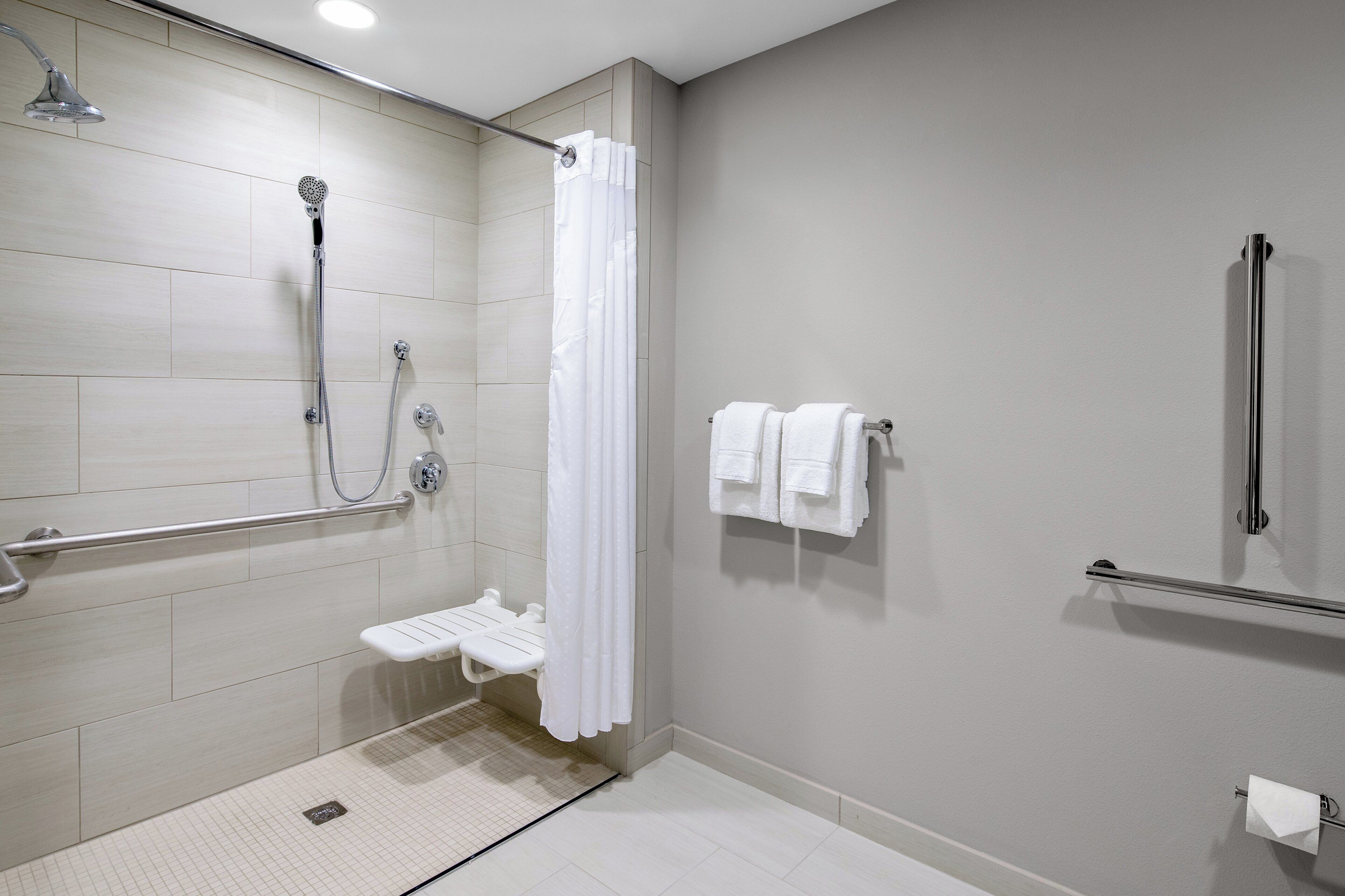 A modern bathroom with a shower, grab bars, a toilet, and a towel rack.