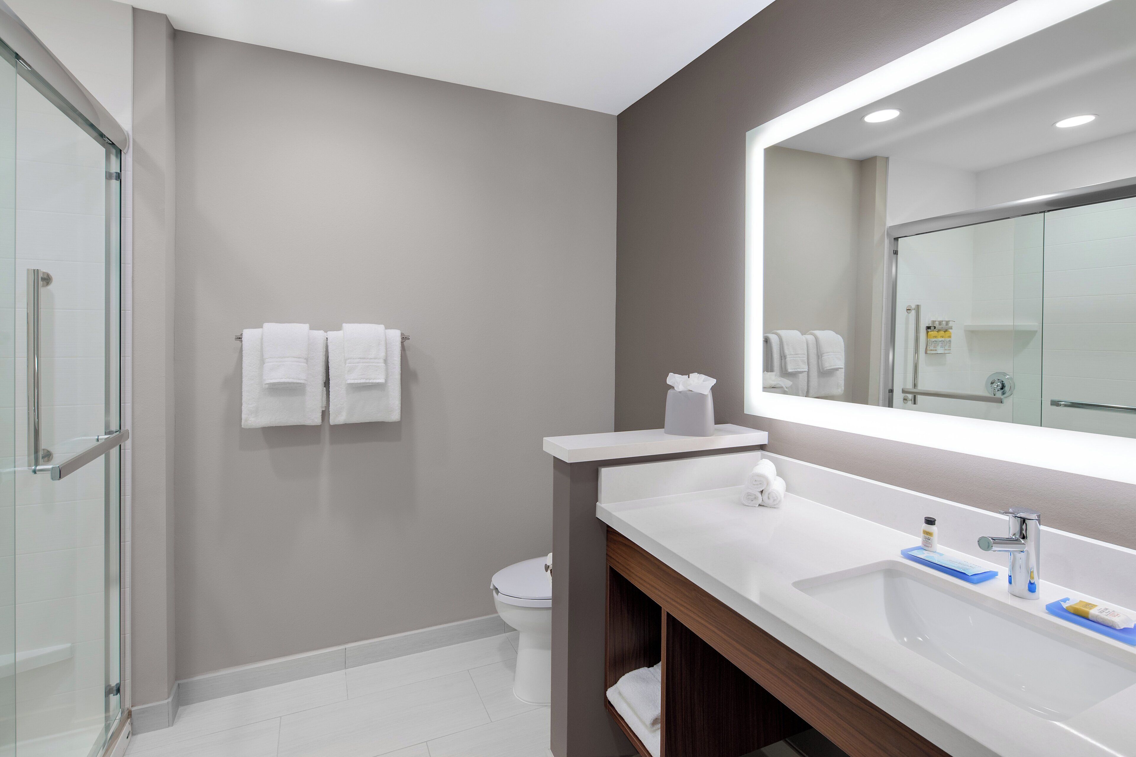 Une salle de bain moderne avec une douche à parois de verre, un lavabo blanc avec un miroir et deux serviettes blanches accrochées au mur.