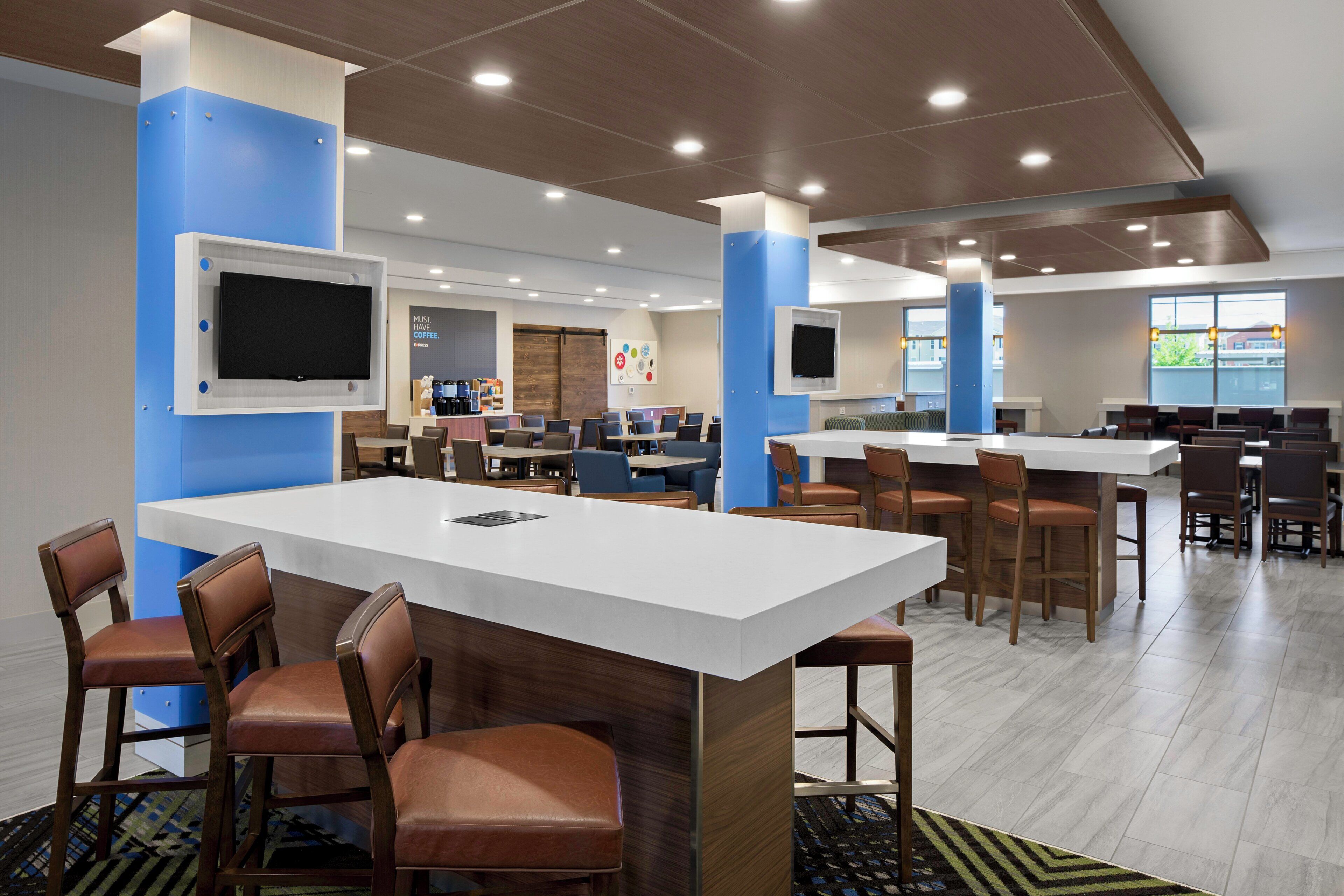 A modern cafeteria with multiple seating areas, including tables and chairs, and a coffee station.