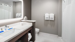 A modern bathroom with a large mirror, white sink, and a shower area.