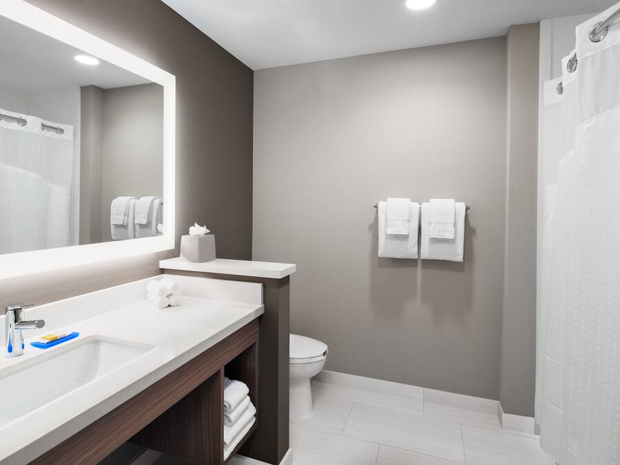 A modern bathroom with a large mirror, white sink, and a shower area.