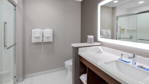 A modern bathroom with a glass shower enclosure, a white sink with a mirror, and two white towels on the wall.