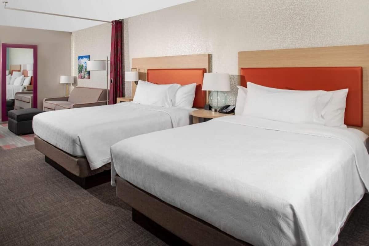 Habitación de hotel con dos camas, una zona de estar y un espejo.