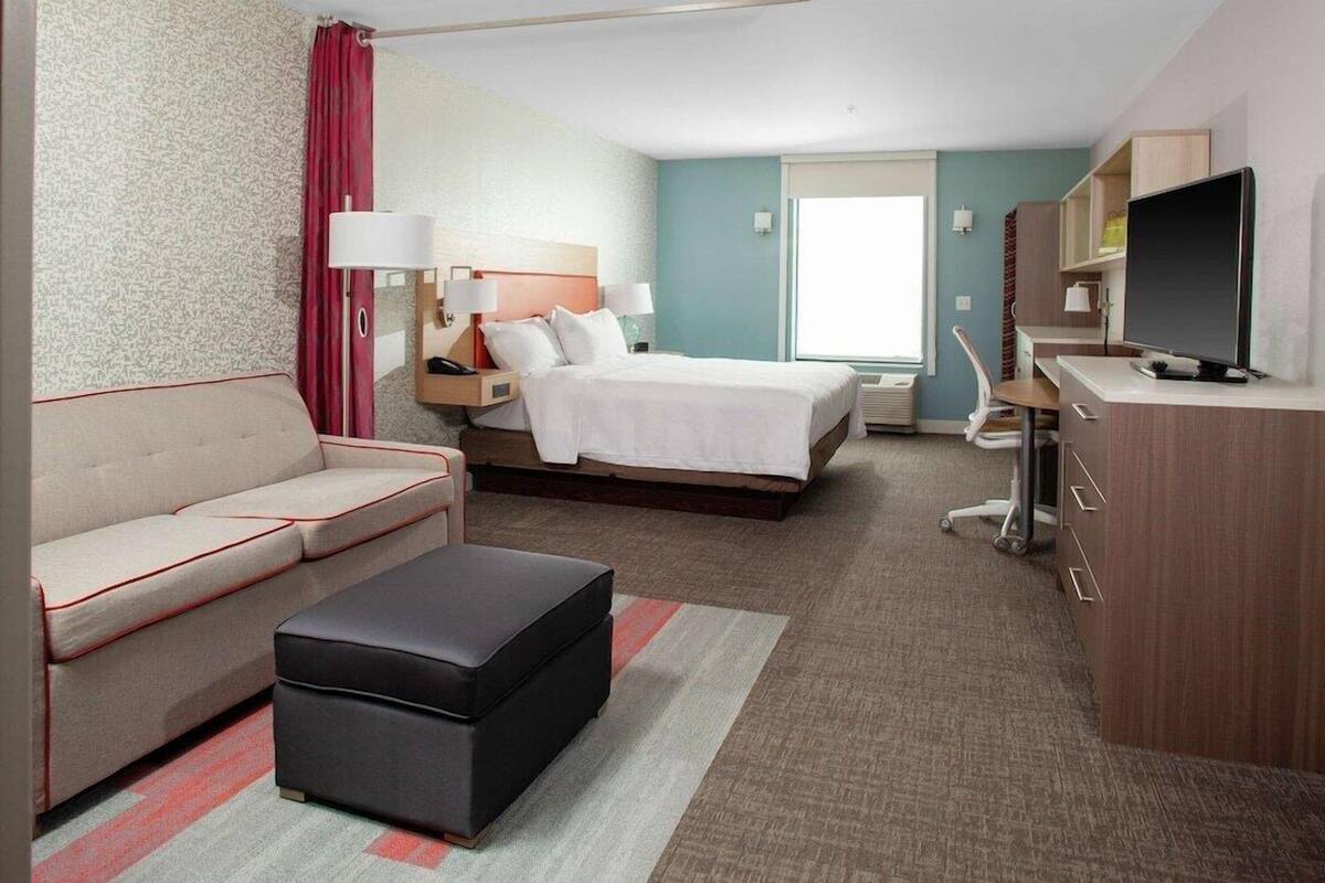 A hotel room with a bed, a sofa, a desk, a TV, and a window.