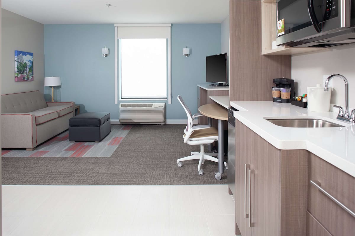 Una sala de estar moderna con sofá, mesa de centro, televisor y área de cocina con pileta y microondas.