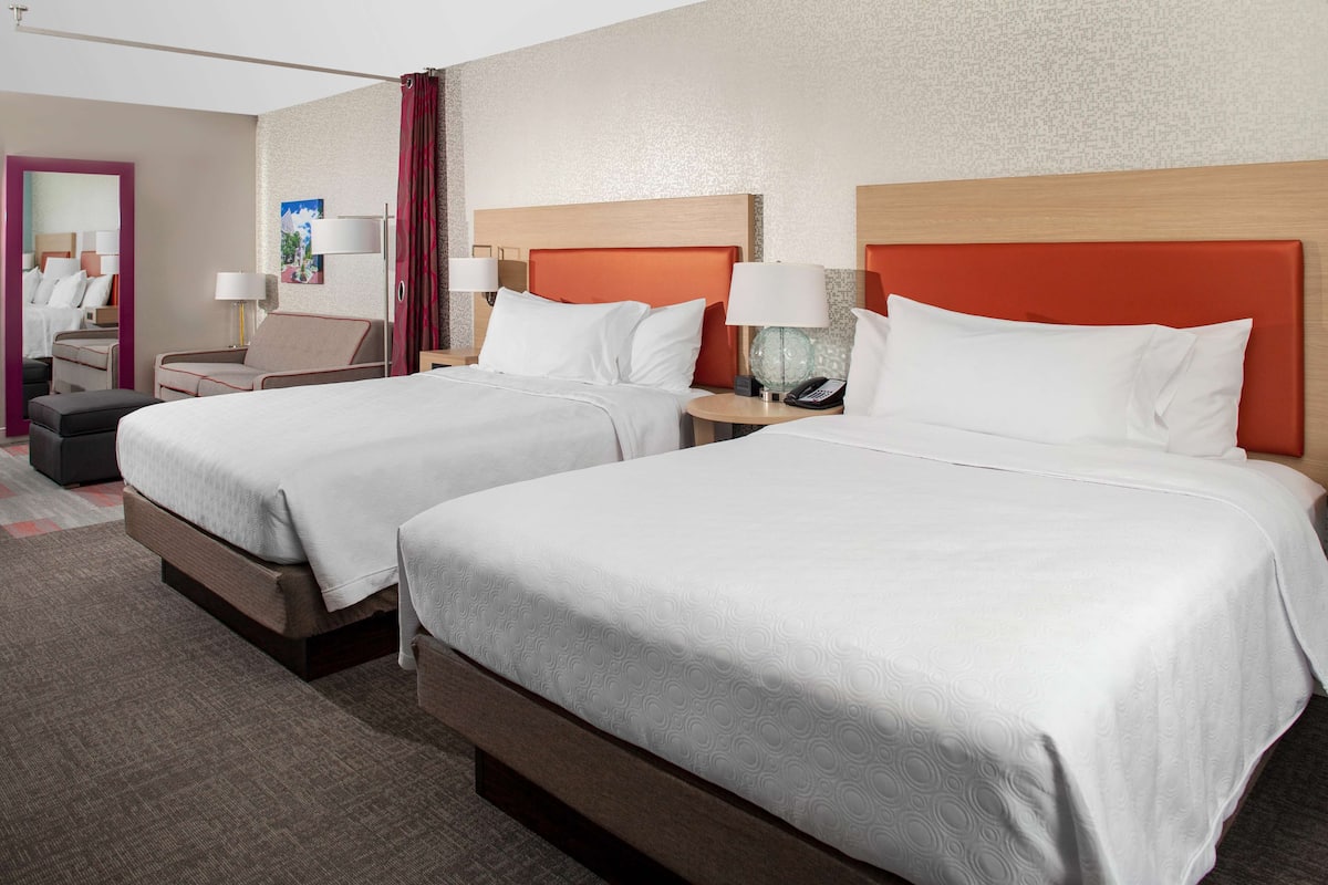 Habitación de hotel con dos camas, una zona de estar y un espejo.