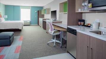 A modern hotel room with a bed, desk, and kitchenette.