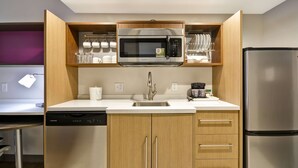 Una cocina compacta con microondas integrado, refrigerador de acero inoxidable y muebles de madera.