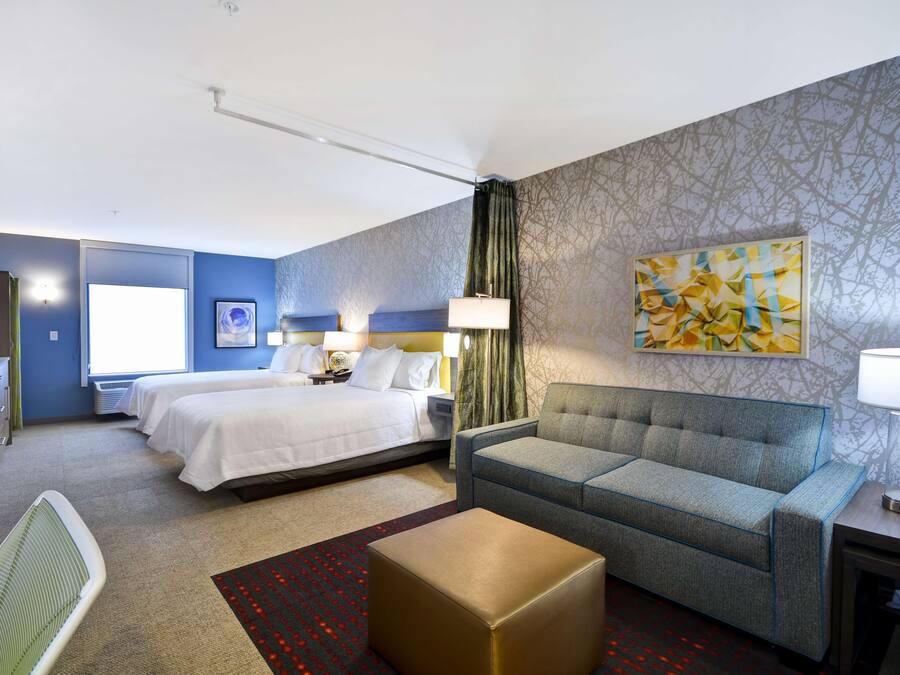 A hotel room with two beds, a sofa, a desk, and a large window.