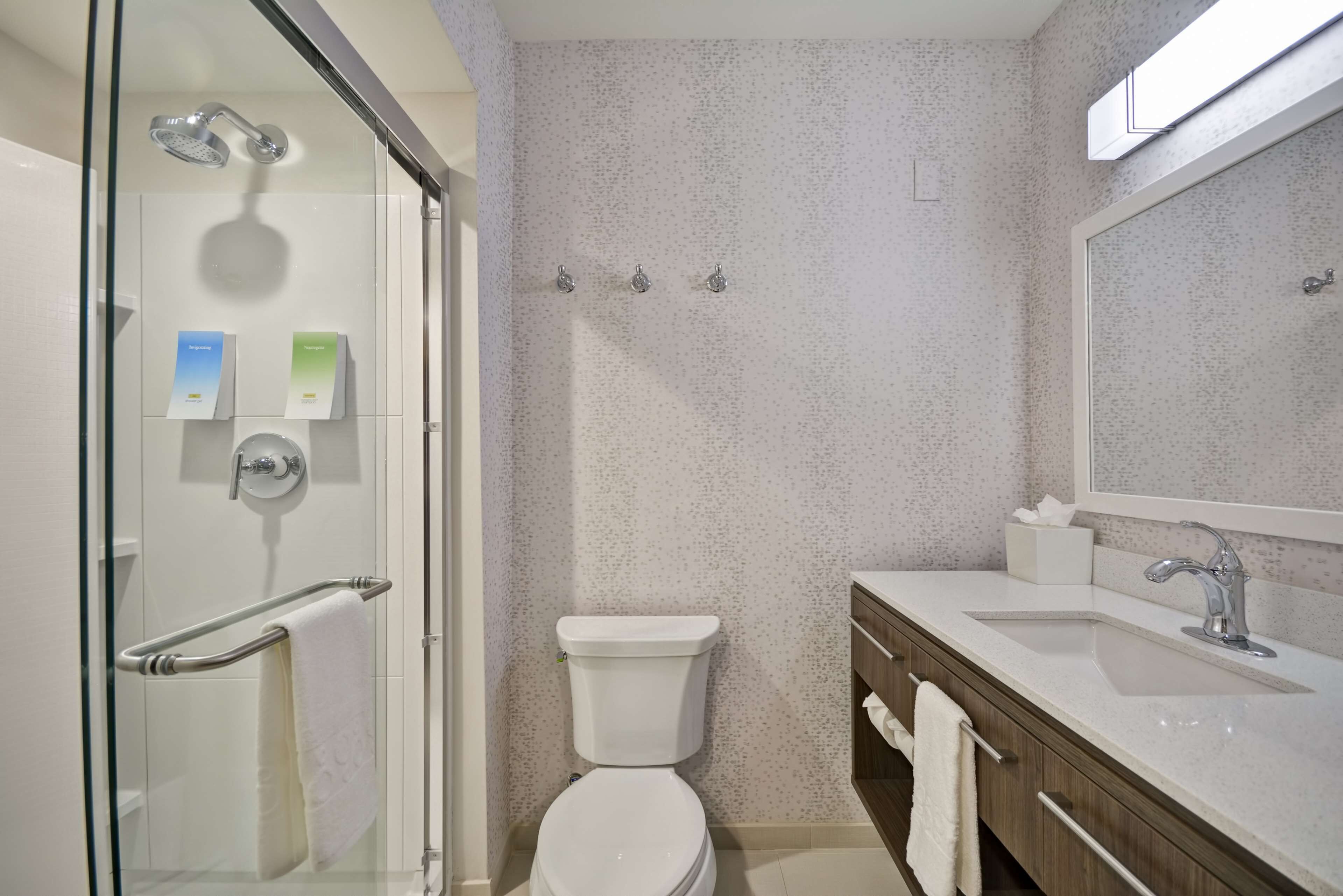 A modern bathroom with a glass shower enclosure, a toilet, a sink with a mirror, and a towel rack.