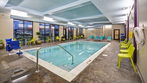 Una piscina interior con paredes de vidrio transparente, sillas amarillas y techo azul.