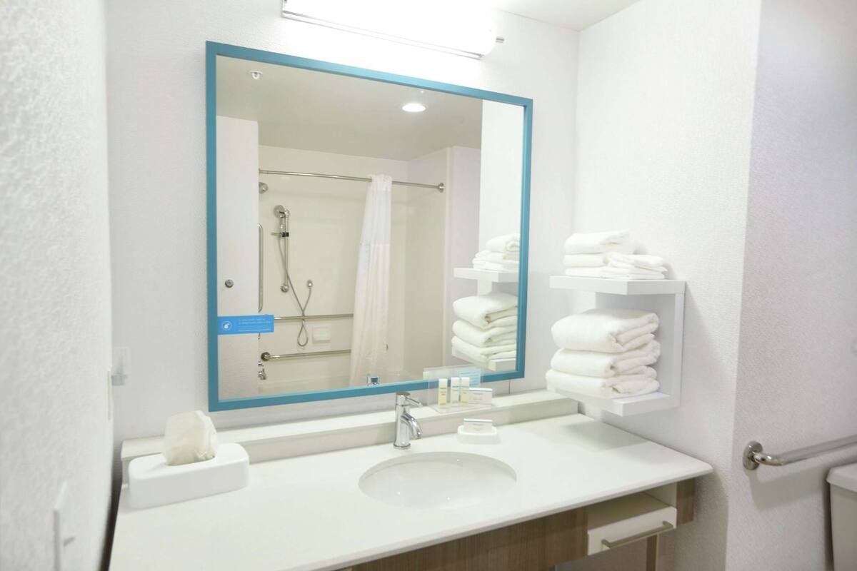 Een badkamer met een wastafel, spiegel, handdoekhouder en een douchehoek.