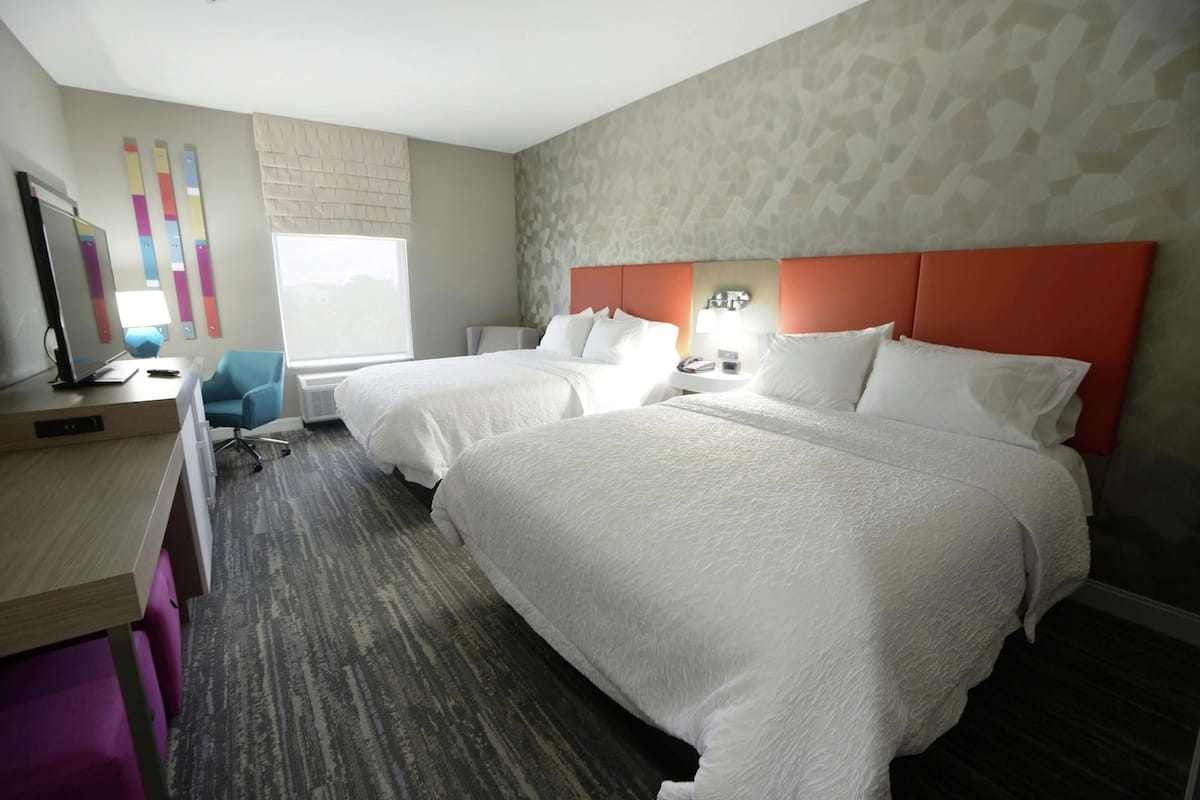 Een hotelkamer met twee bedden, een bureau, een stoel, een televisie en een raam.