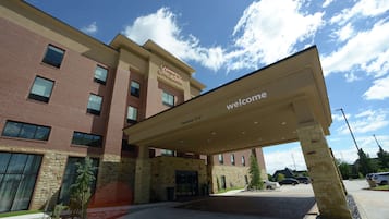 A hotel entrance with a 'Welcome' sign, a clear sky, and a parking lot.