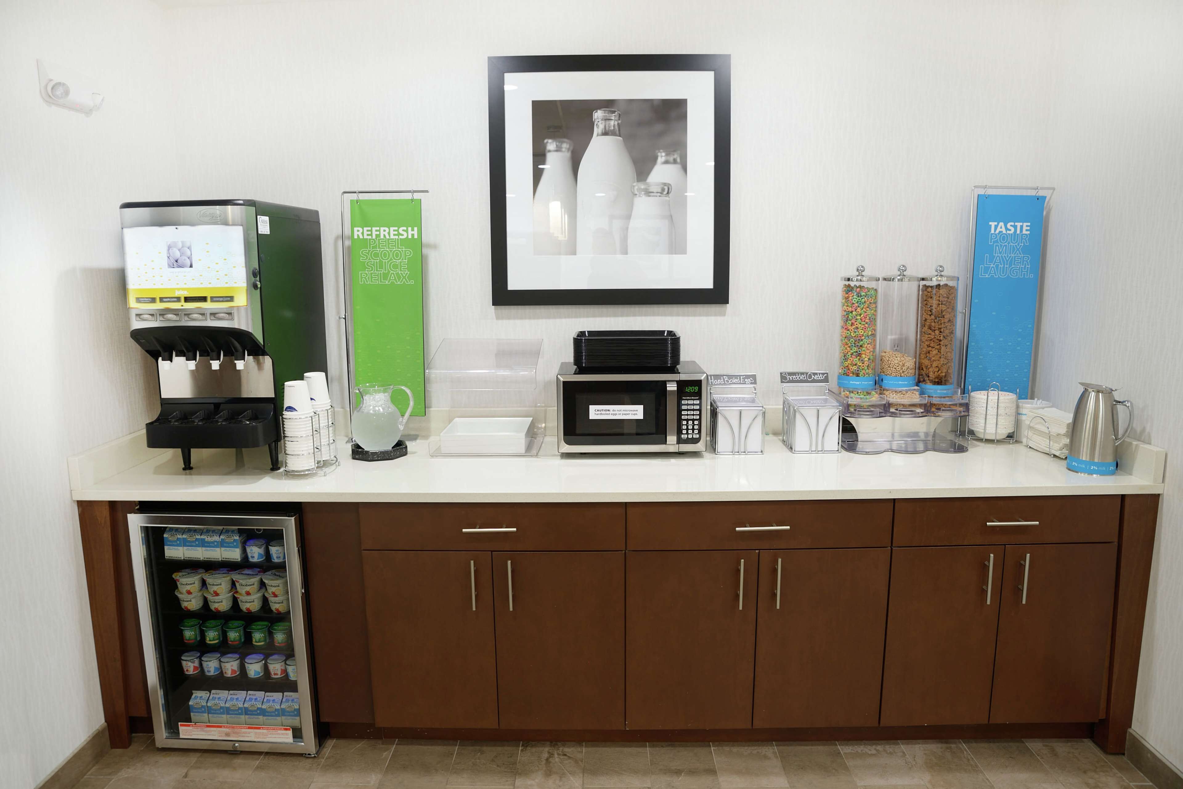 Een kitchenette met een koffiezetapparaat, magnetron, koelkast en diverse bakjes voor levensmiddelen.