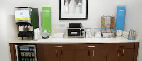 A kitchenette with a coffee machine, microwave, refrigerator, and various food containers.