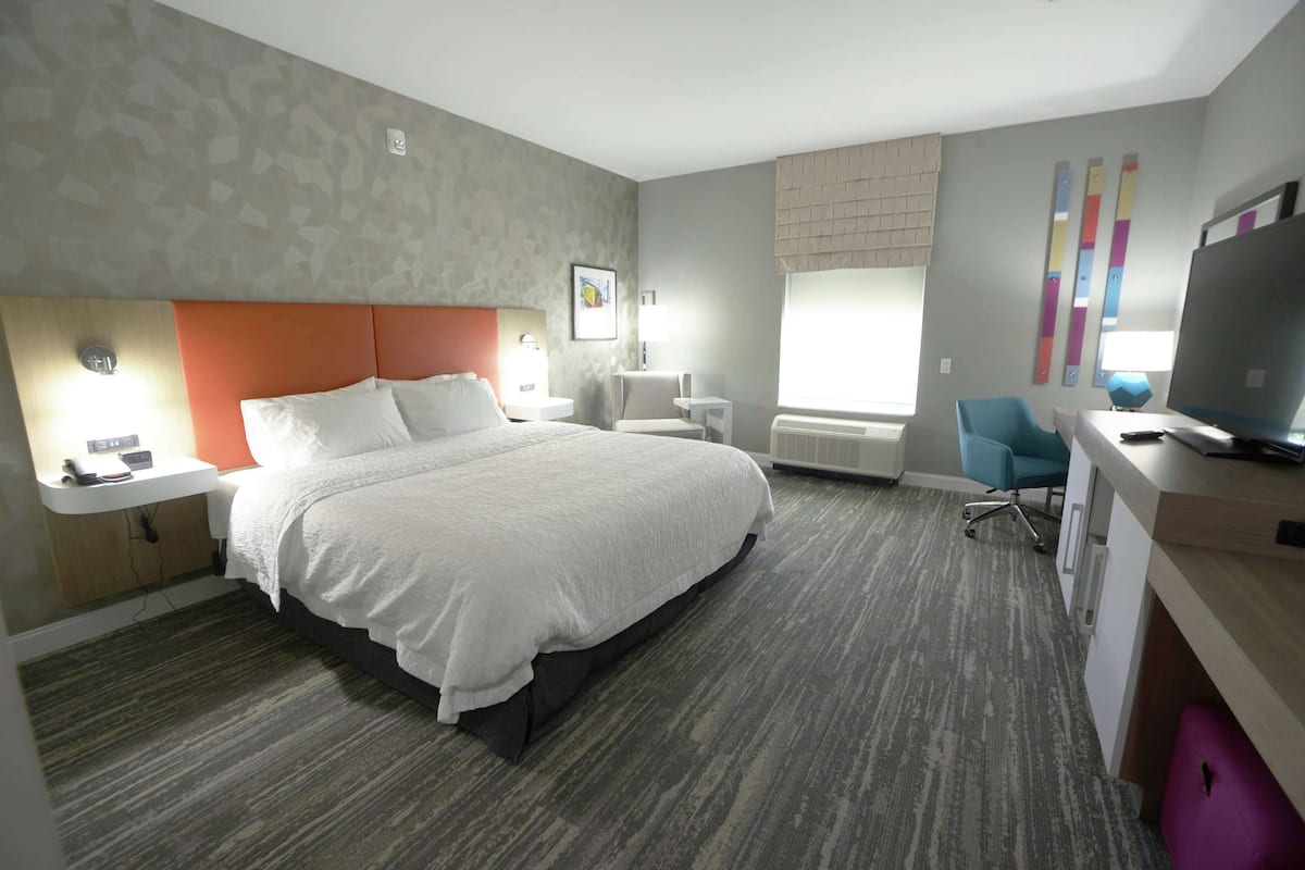 Een hotelkamer met een groot bed, een bureau met computer, een stoel, een raam met zonwering en een wandtelevisie.