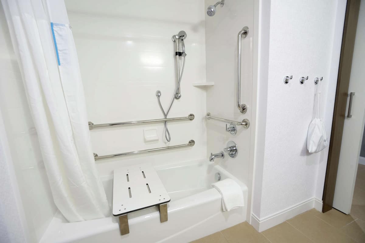 Een moderne badkamer met een inloopdouche, handgrepen, een zitje en een handdoekrek.