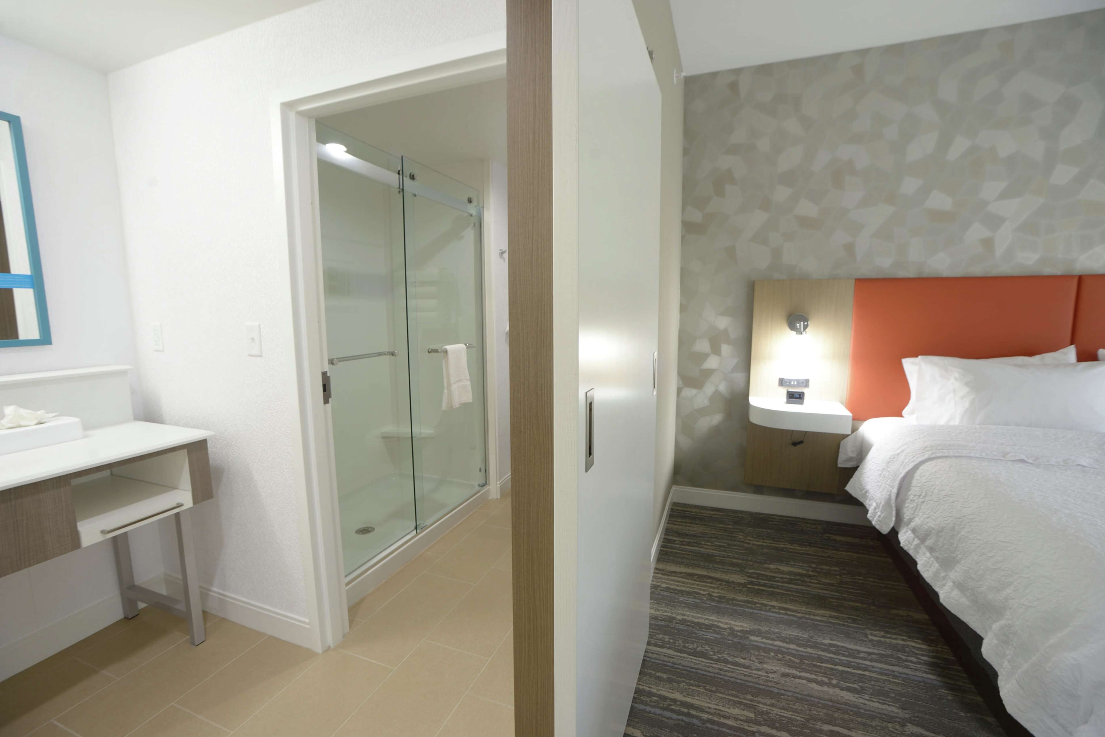 A hotel room with a bed, a desk, a glass-enclosed shower, and a patterned wall.