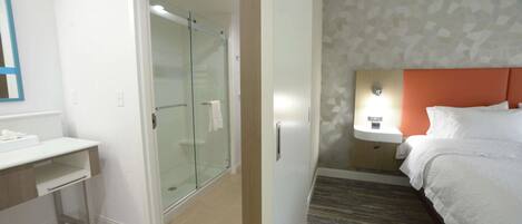A hotel room with a bed, a desk, a glass-enclosed shower, and a patterned wall.