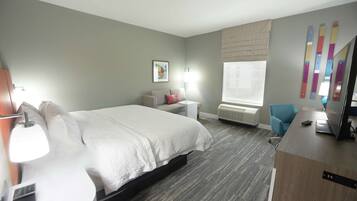 A hotel room with a bed, bedside table, lamp, chair, desk, and a TV.