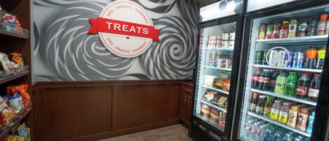 A grocery store with a 'Treats' sign on the wall, refrigerated beverage cases, and shelves stocked with snacks and groceries.