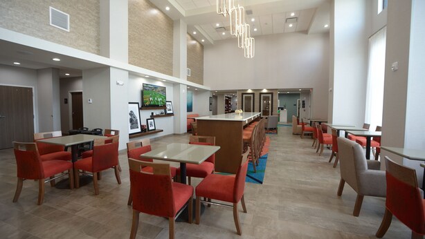 A spacious dining area with multiple tables and chairs, a long counter, and a television mounted on the wall. - Hampton Inn & Suites Oklahoma City/Quail Springs (Oklahoma City)