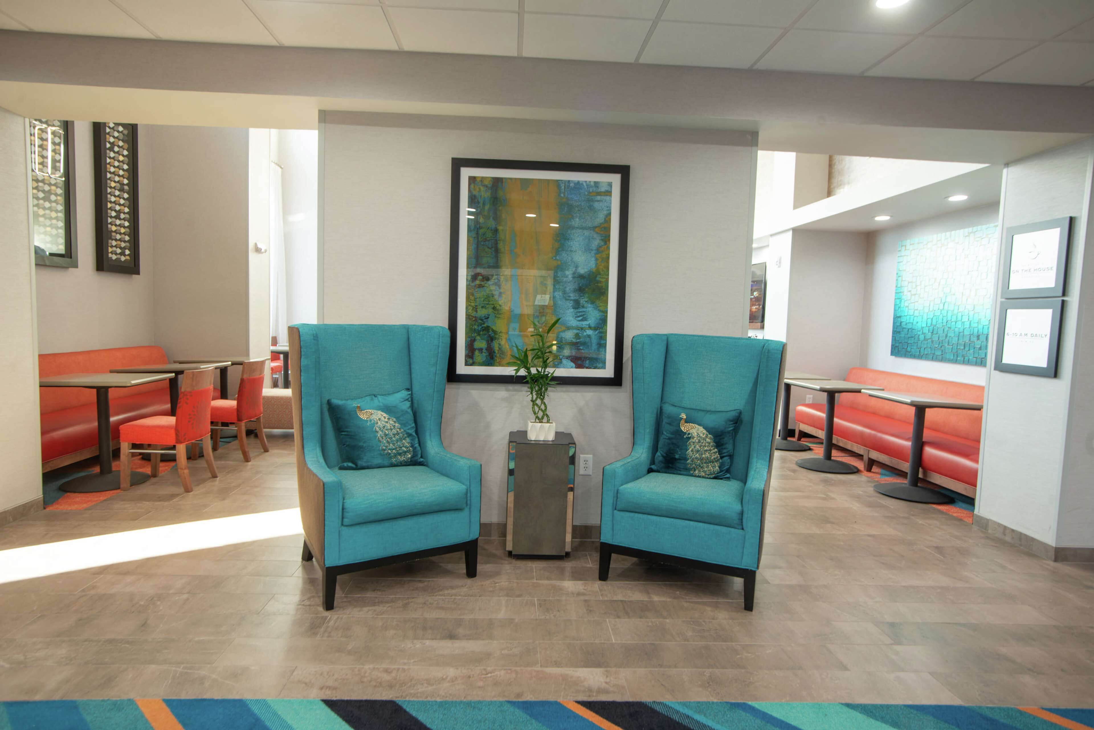 A lobby with teal armchairs, red seating, and a large abstract painting on the wall.