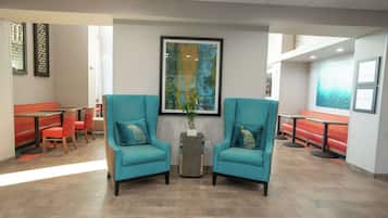 A lobby with teal armchairs, red seating, and a large abstract painting on the wall.