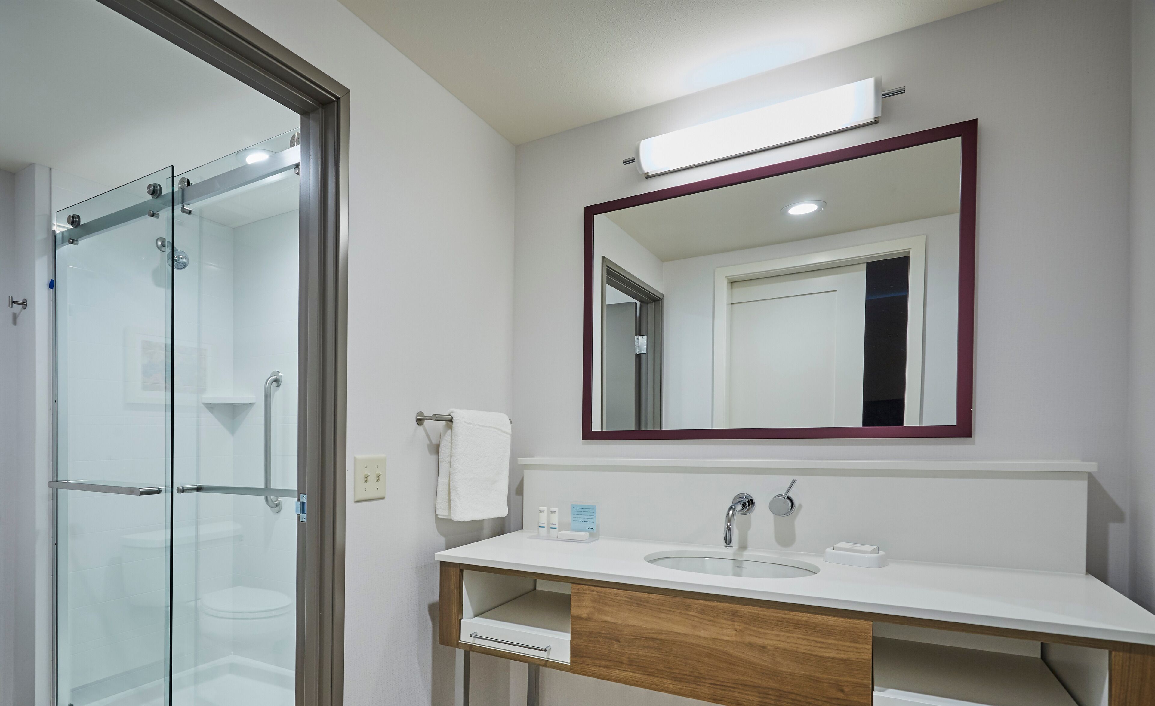 A modern bathroom with a glass shower enclosure, a white sink with a wooden vanity, and a large mirror above the sink.