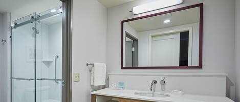 A modern bathroom with a glass shower enclosure, a white sink with a wooden vanity, and a large mirror above the sink.