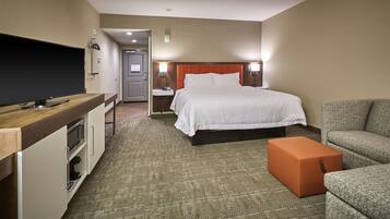 A hotel room with a bed, a TV, a sofa, and a small orange ottoman.