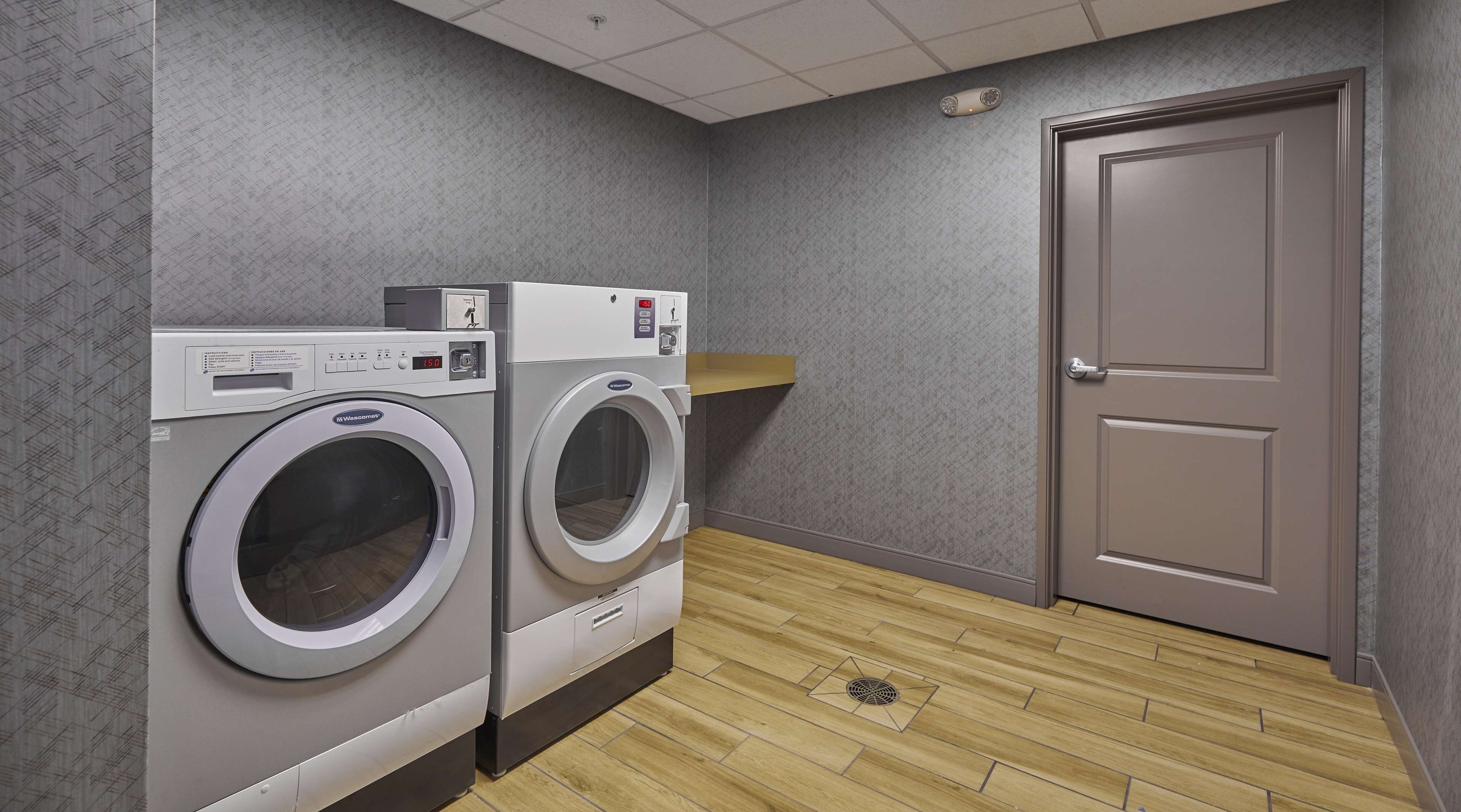 A laundry room with two front-loading washing machines, a control panel, and a door.
