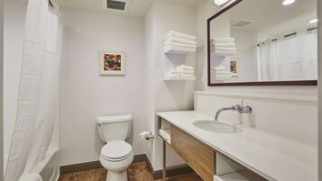 Une salle de bain moderne avec des toilettes, un lavabo et un espace douche. On peut voir des serviettes sur une étagère et un tableau encadré au mur.