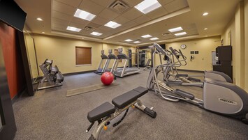 Uma academia com esteiras, elípticos, um banco e uma bola de exercício vermelha.