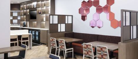 A modern restaurant with wooden tables and chairs, a large TV, and a wall with hexagonal mirrors.