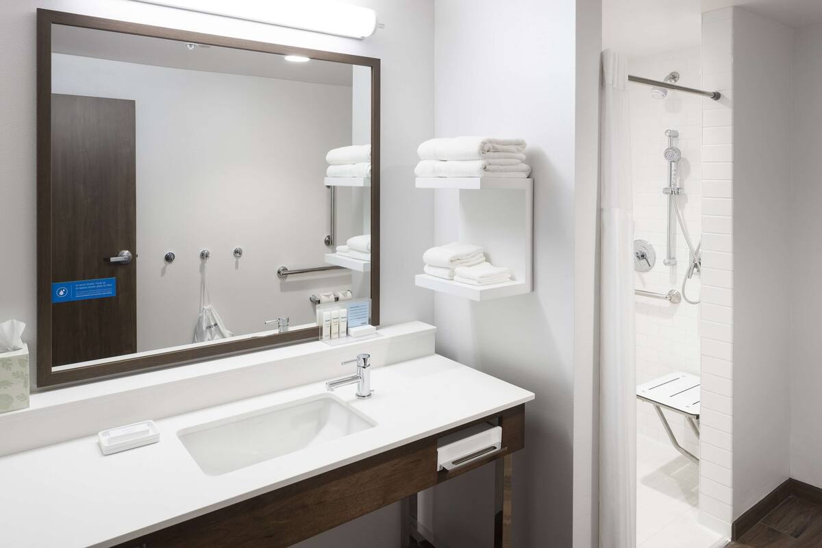 A modern bathroom with a large mirror, white sink, and a shower area.