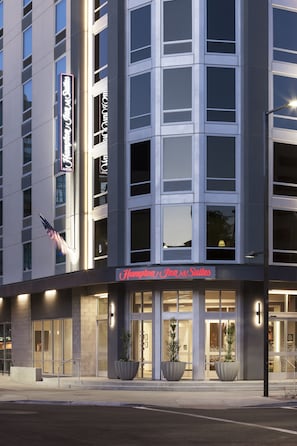 Un hôtel moderne, reconnaissable à son enseigne où l’on peut lire « Hampton Inn & Suites ».